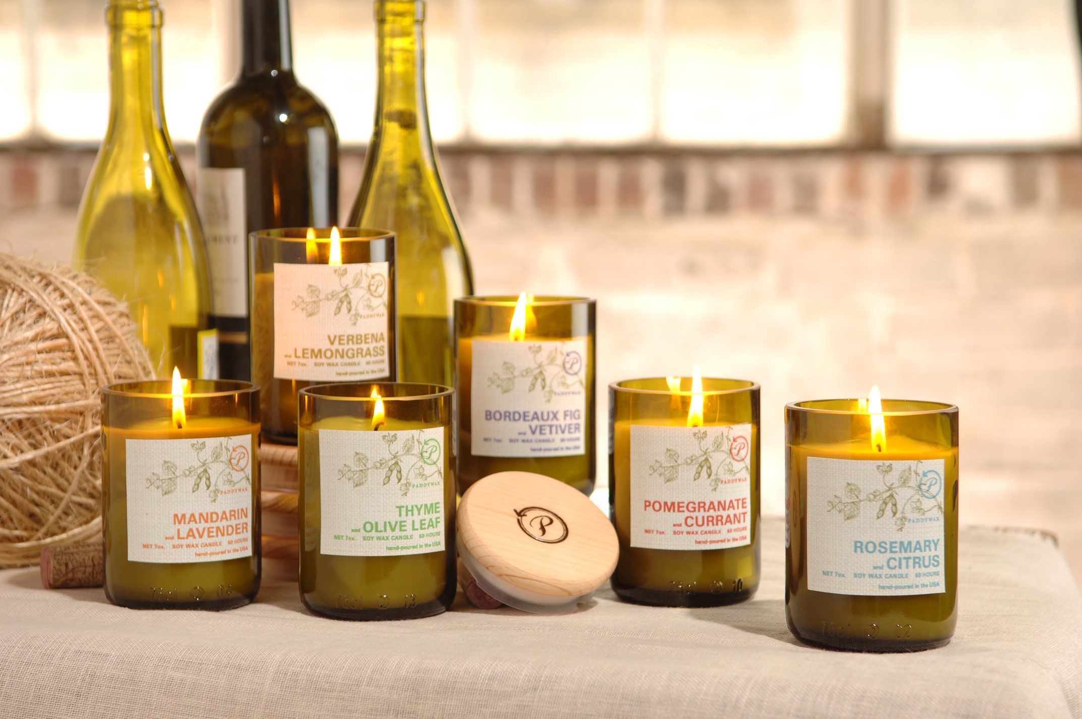 Home fragrance. Six lit candles in a row. Each candle has been made using the bottom half of a wine bottle.