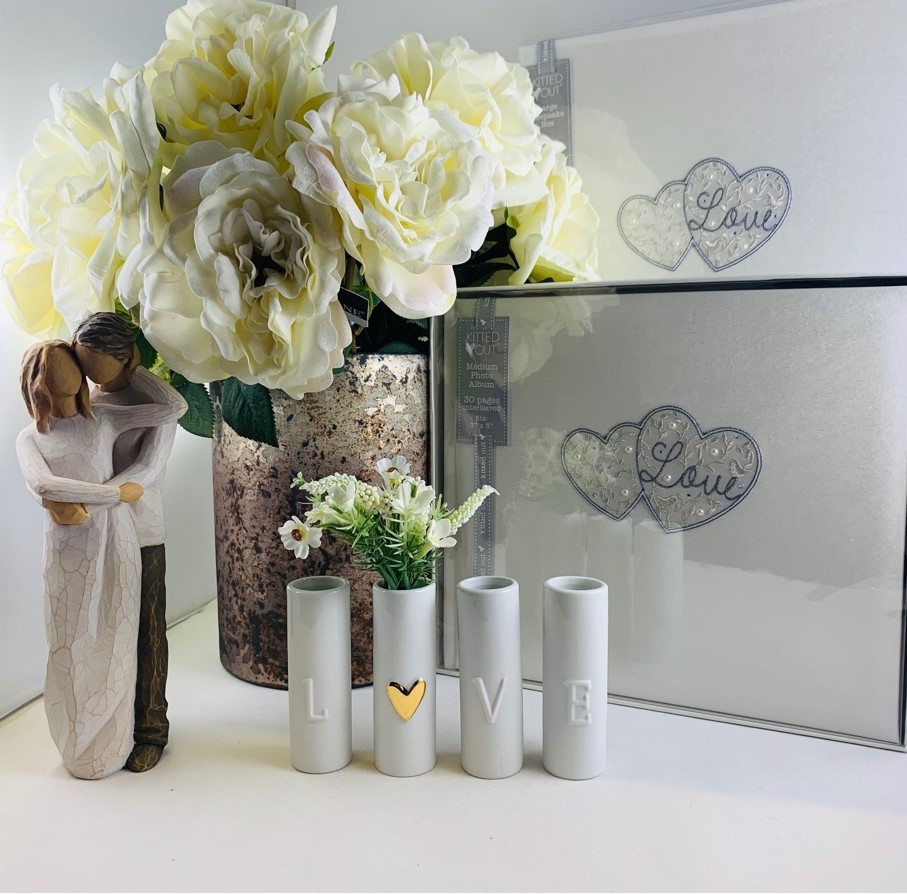 Wedding gifts. Image of a vase of white flowers, four small white posey vases and a statuete of a man holding a woman in white.
